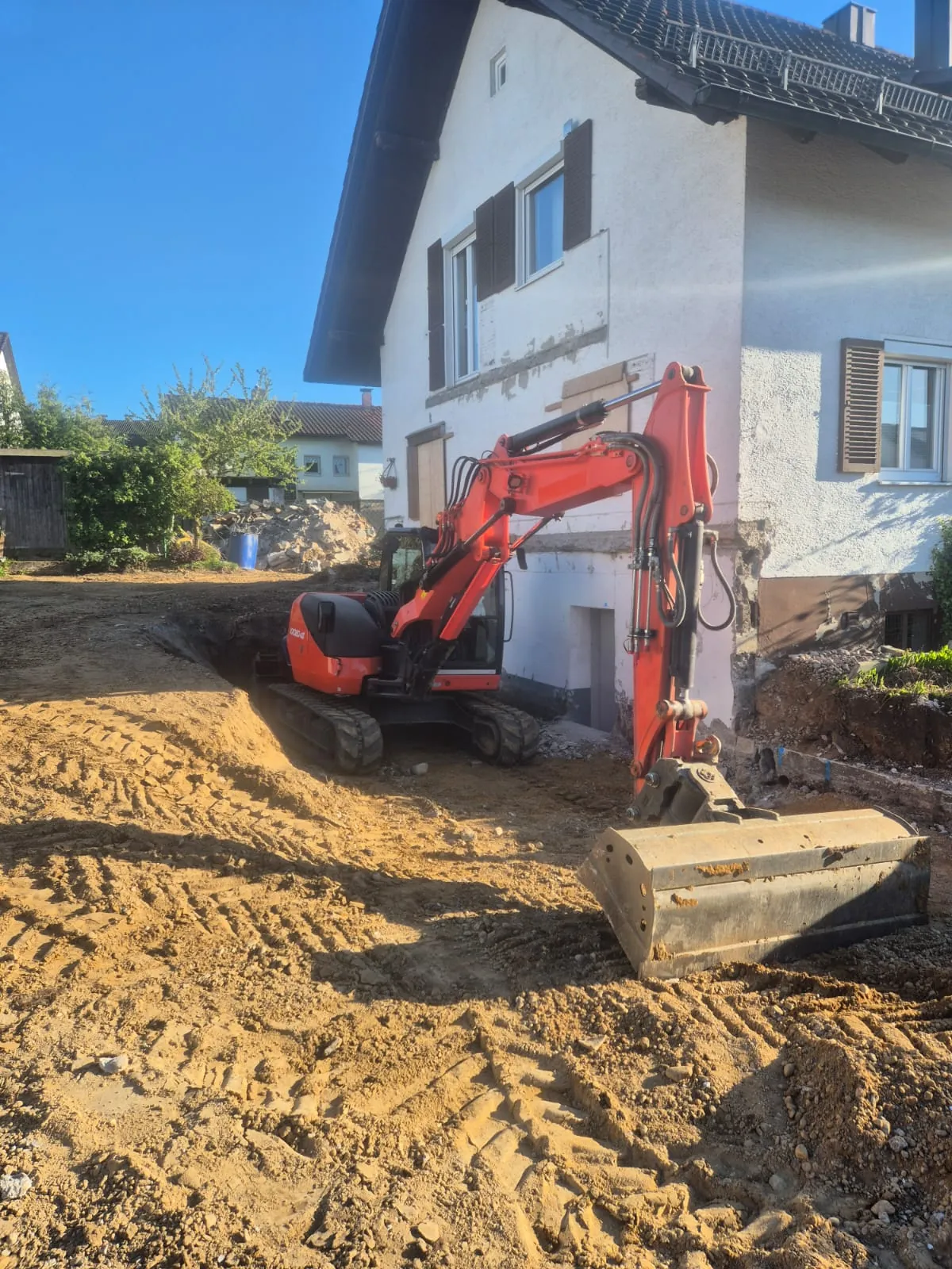 Bagger hebt ein L-Stein-Betonteil vor einem Wohnhaus ein