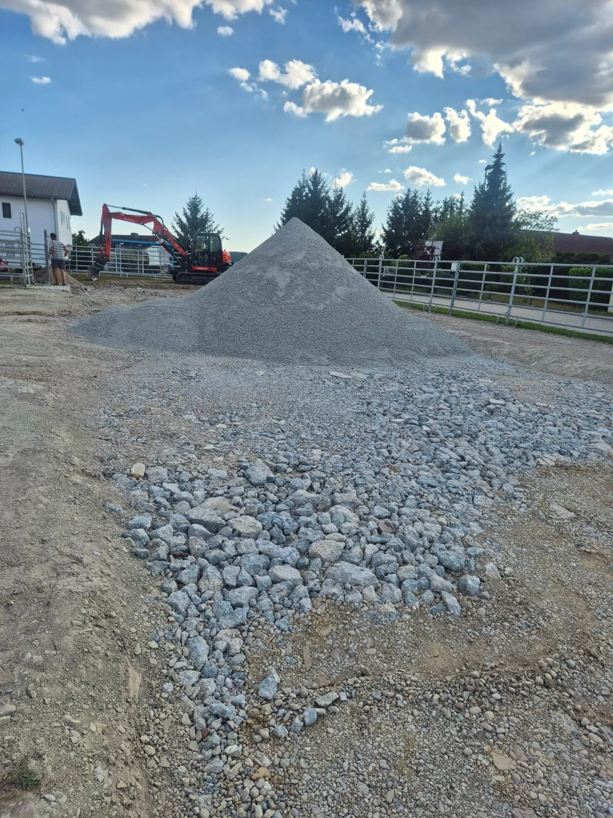Schotter wird auf der Hoffläche verteilt, im Hintergrund der Bagger