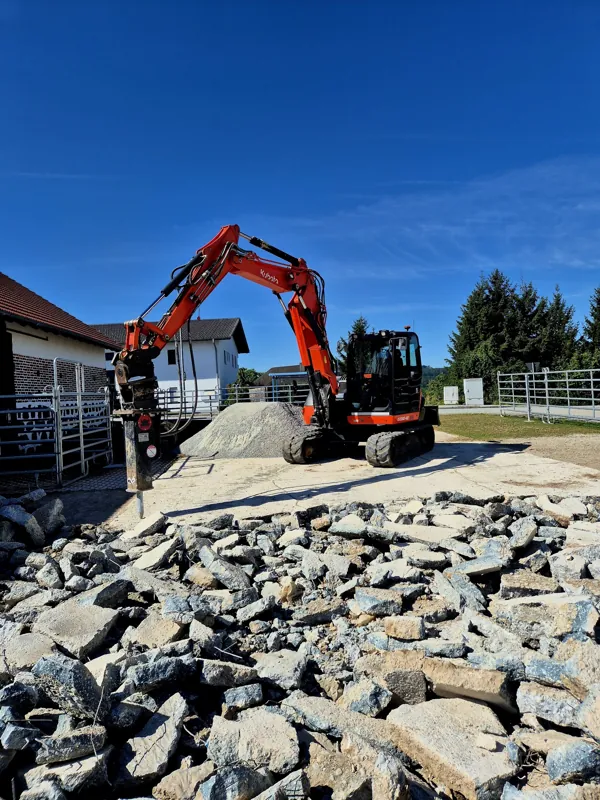 Bagger setzt große Wasserbausteine vor einem Haus